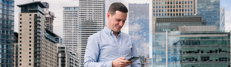 A smiling person looks at their phone with Canary Wharf skyscrapers in the background