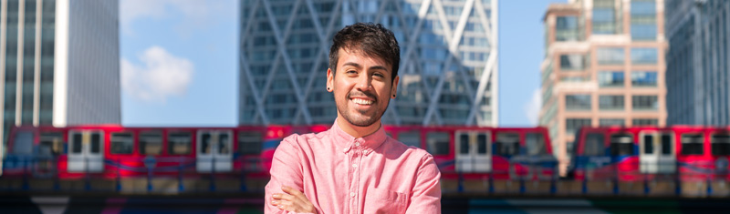 A smiling person with Canary Wharf skyscrapers and a DLR train in background