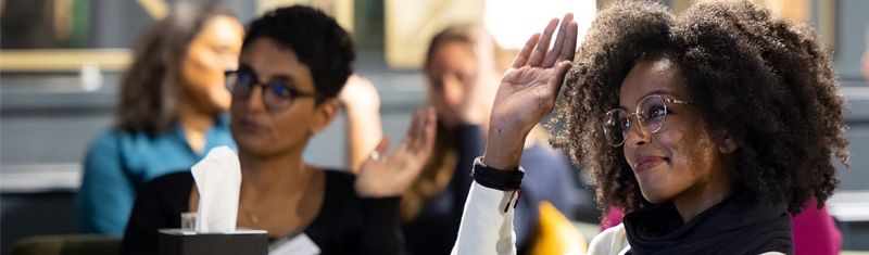 A smiling person with their hand raised at a business event 