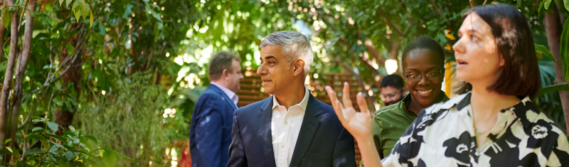 Sadiq Khan and a group of people walk through a garden filled with greenery
