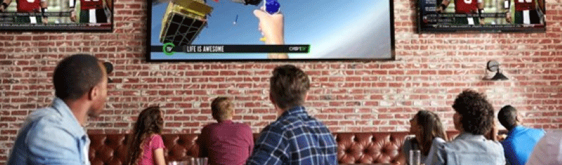 People in a bar watching sports and a commercial on multiple TVs, brick wall background.