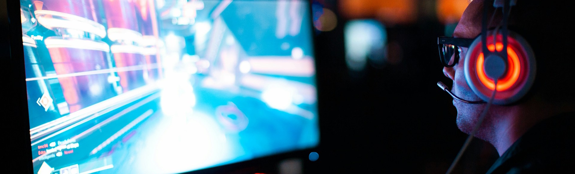 Man with headset wearing glasses playing game on a computer.