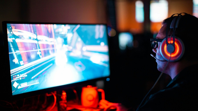 Man with headset wearing glasses playing game on a computer.