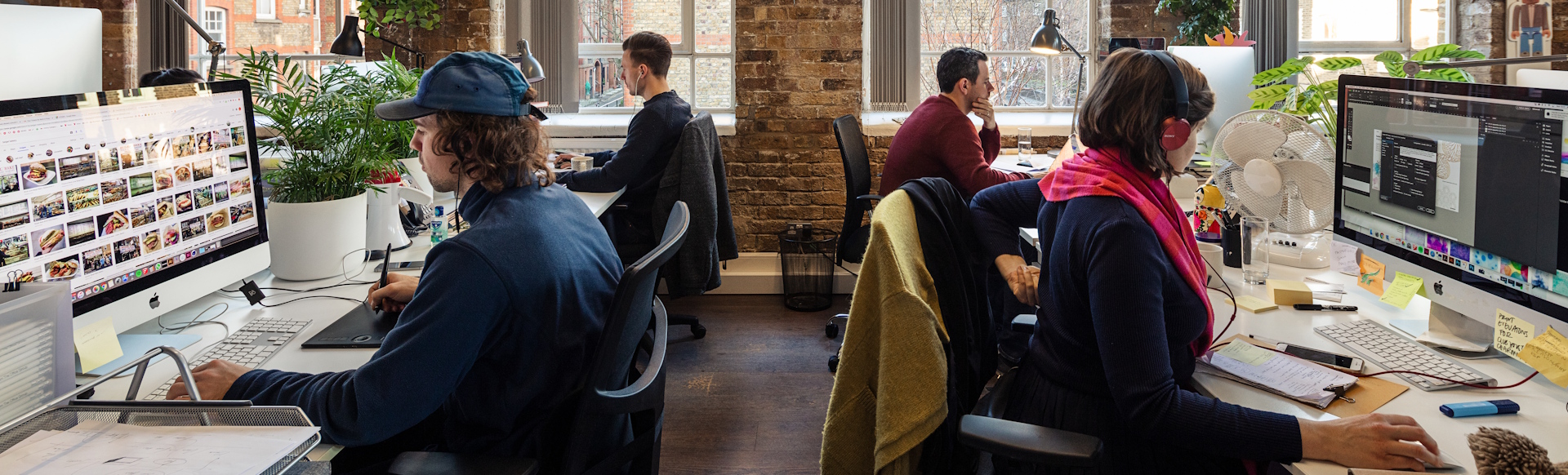 Four people working on computers in shared office space in Shoreditch, complete with big windows and brick walls.