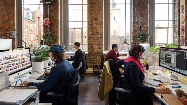 Four people working on computers in shared office space in Shoreditch, complete with big windows and brick walls.