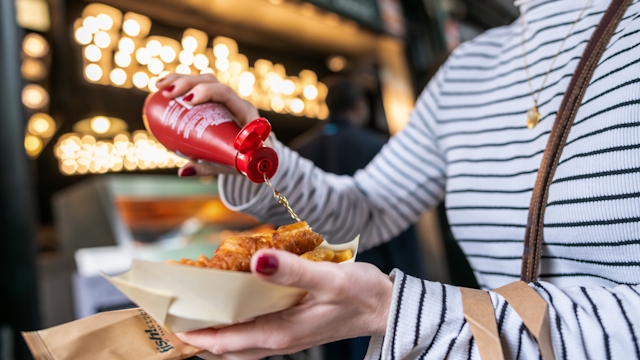 Woman holding plastic-free street food packaging with fish and chips.