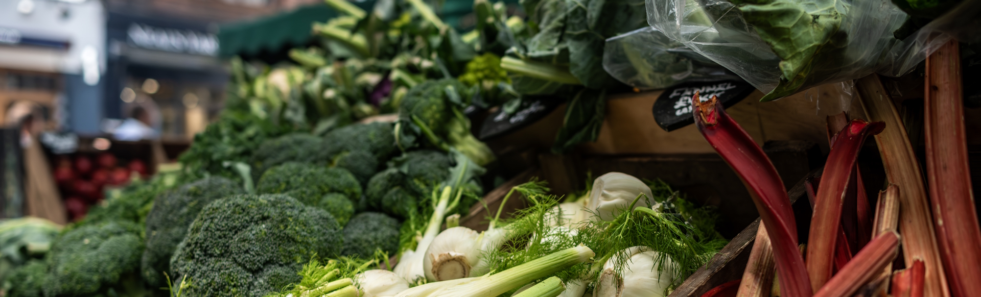Close-up of green vegetables and rhubarb on market stall.