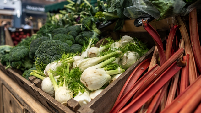 Close-up of green vegetables and rhubarb on market stall.