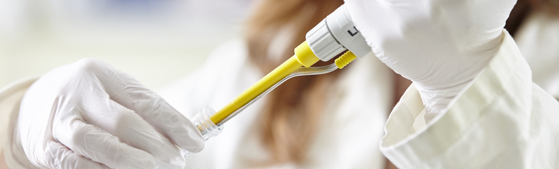 Woman scientist with white gloves handling a pipette.