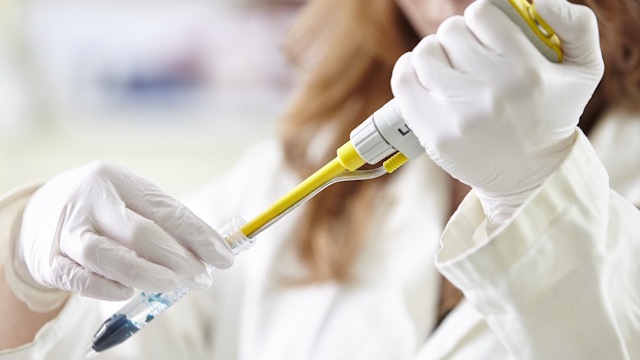 Woman scientist with white gloves handling a pipette.