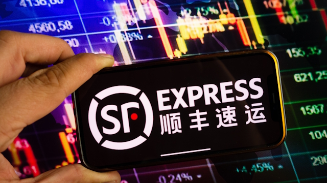 Close up of a phone with SF Express written on it in English and in Chinese, with stock markets in the background.