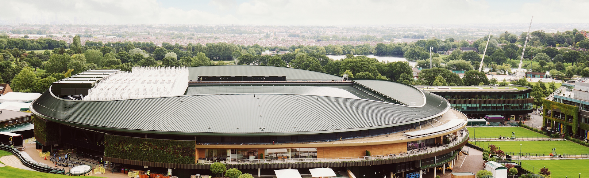 Wimbledon stadium viewed from afar with greenery and London skyline in the background.