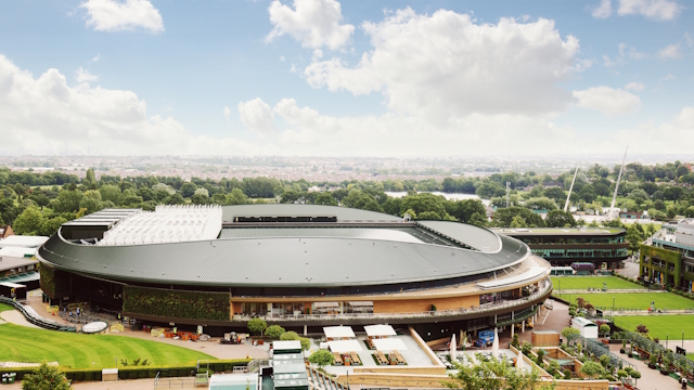 Wimbledon stadium viewed from afar with greenery and London skyline in the background.