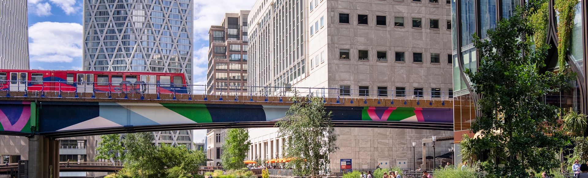Canary Wharf cityscape with colourful train, buildings and trees.