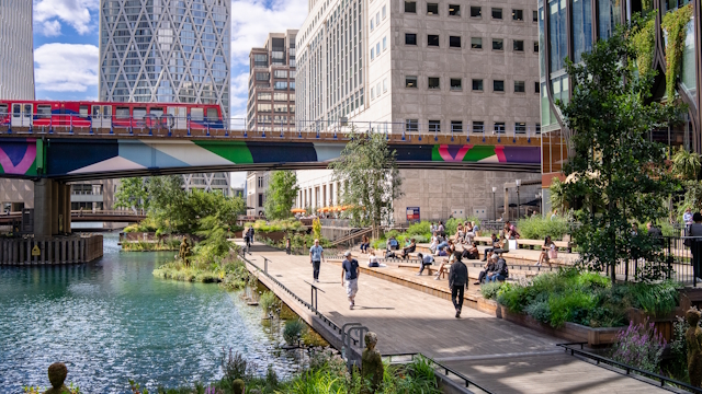 Canary Wharf cityscape with colourful train, water, buildings and trees.