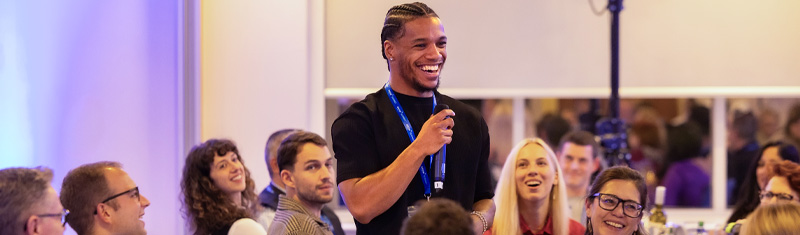 A man standing in front of people sitting on tables at a business event. 