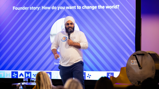 A man standing on a stage at a business event speaking to a crowd of people.