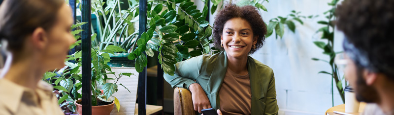 A group of people sitting at a coffee table talking and smiling surrounded by plants.