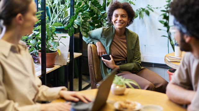 A group of people sitting at a coffee table talking and smiling surrounded by plants.