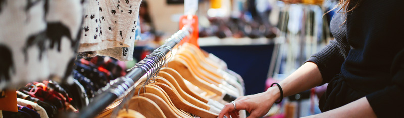 A close up of a woman's hands browsing through a clothes stall in a market.