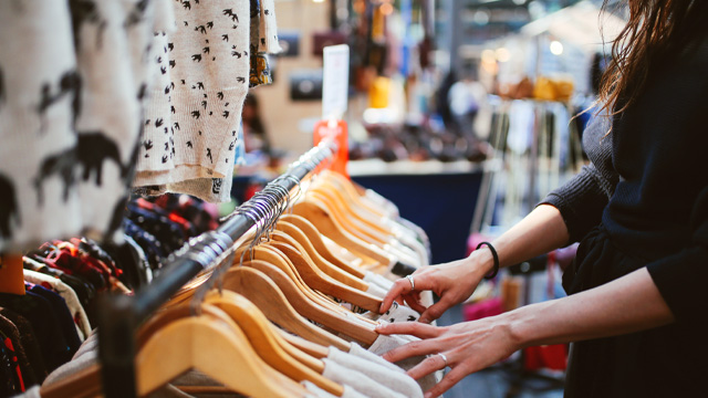 A close up of a woman's hands browsing through a clothes stall in a market.