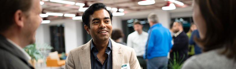 A smiling man in business attire speaking with two people at a networking event.