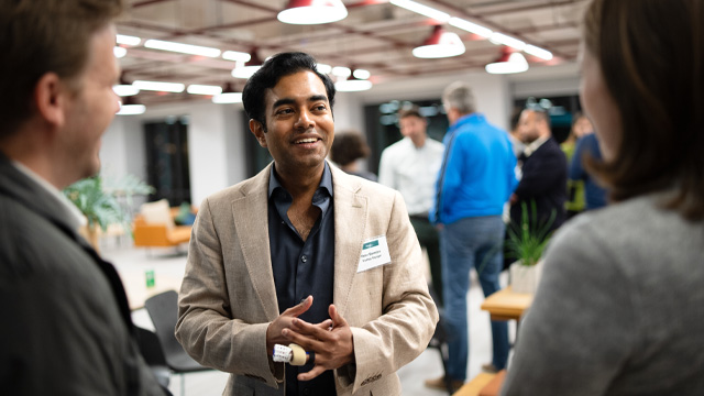 A smiling man in business attire speaking with two people in a networking event.