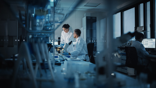 Three people in white lab coats working in a research lab.