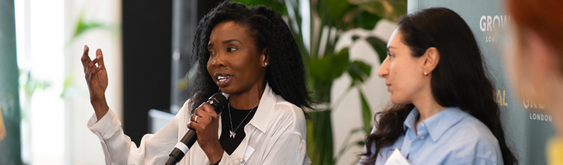 A woman with a microphone speaking to an audience in a business event.
