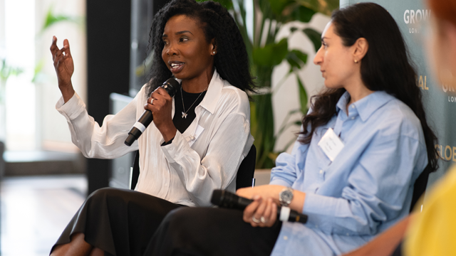 A woman with a microphone speaking to an audience during a business event. 