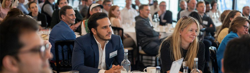 A room full of people sitting on tables at a business event.