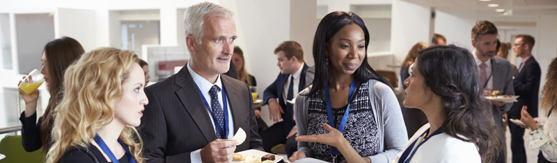 Four people networking at an event with more people in the background.