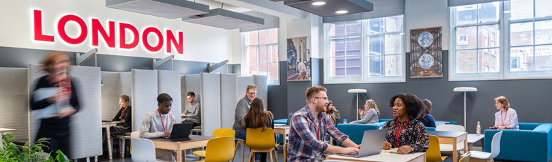 A view of an office collaborative space with tables and sofas and people working and talking