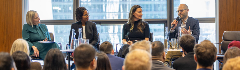 A group of four panelists talking to a crowd at a business conference event. 