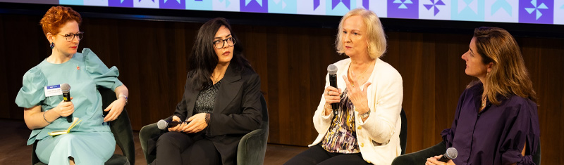 Four women in business attire sitting as a panel at a business event speaking to an audience out of frame.
