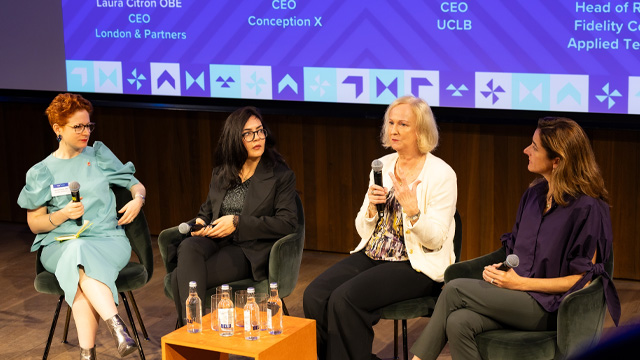 Four women in business attire sitting as a panel at a business event speaking to an audience out of frame.