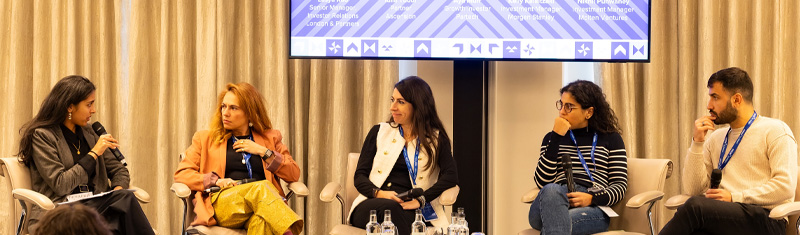 Four women and a man in business attire sitting as a panel at a business conference.