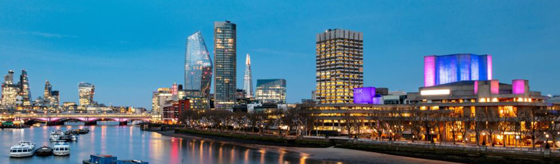 An evening view of the River Thames overlooking the Southbank district with illuminated buildings.