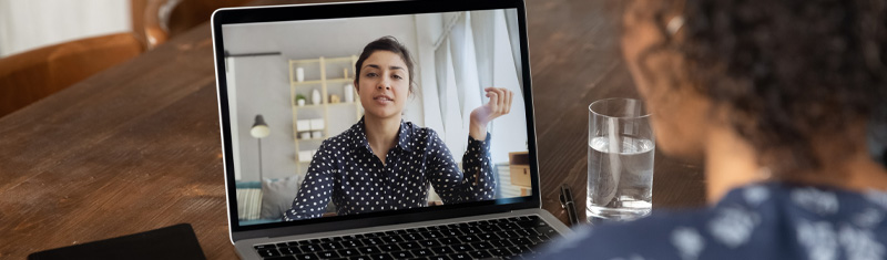 A woman sitting at a table in a video call with another woman on a laptop.