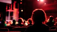 Red lights washing over audience members facing the stage.