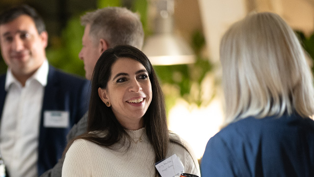 A smiling woman networking surrounded by people in a business event.