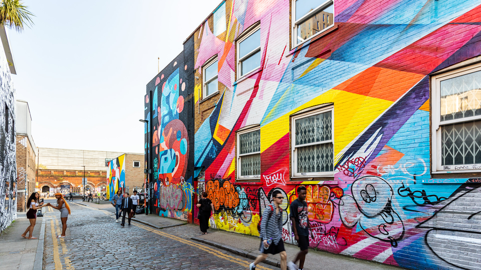 People walking on a cobbled street with buildings covered in bright rainbow coloured graffiti