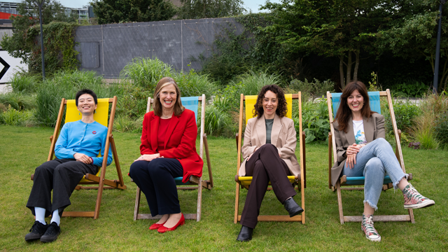 Four women smiling to the camera and sitting on deck chairs in a garden.