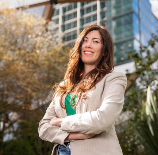 A woman with folded arms smiling with office buildings in the background
