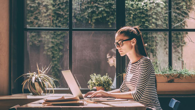  A woman working on a laptop sitting next to a window
