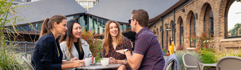A group of four people sitting outdoors in a table drinking coffee and chatting.