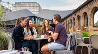A group of four people sitting outdoors in a table drinking coffee and chatting.