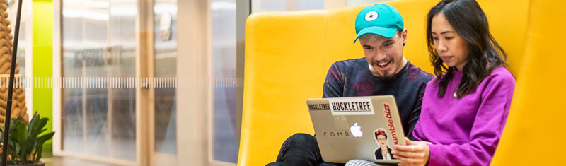 A man and a woman working on a laptop sitting on a yellow sofa