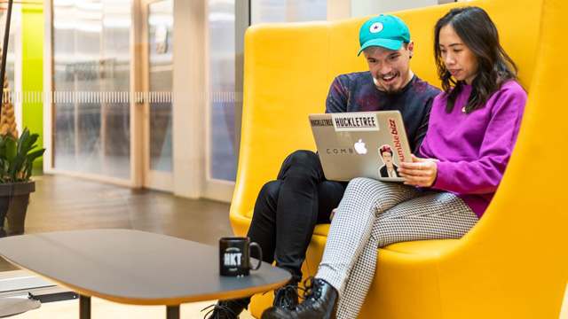 A man and a woman working on a laptop sitting on a yellow sofa.
