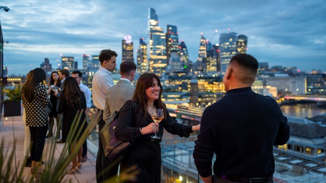 A group of young professionals chat in front of the London skyline.